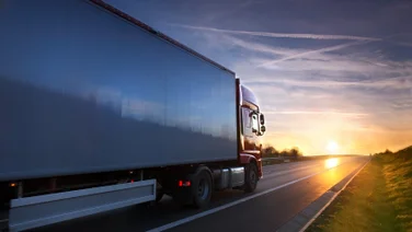 A large red truck drives toward the sunset on open road