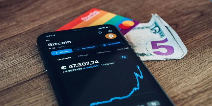 bitcoin on phone with card and cash underneath