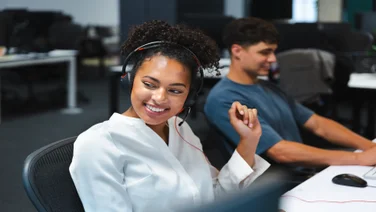 Two smiling colleagues on headsets. Source: Tech.co