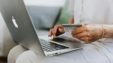 A person holds a credit card in front of a laptop