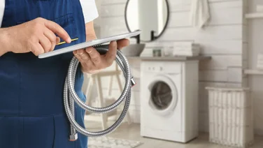 A plumber uses a tablet computer while holding a hose in a neutral bathroom.