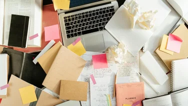 Papers piled around a laptop