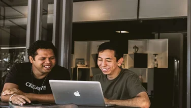 two men smiling at a laptop in a small office