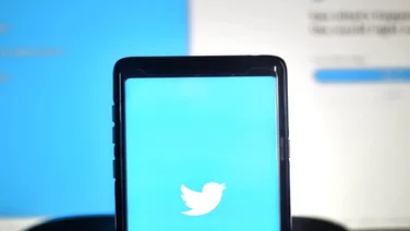 The Twitter logo on a smartphone, being held in front of a screen