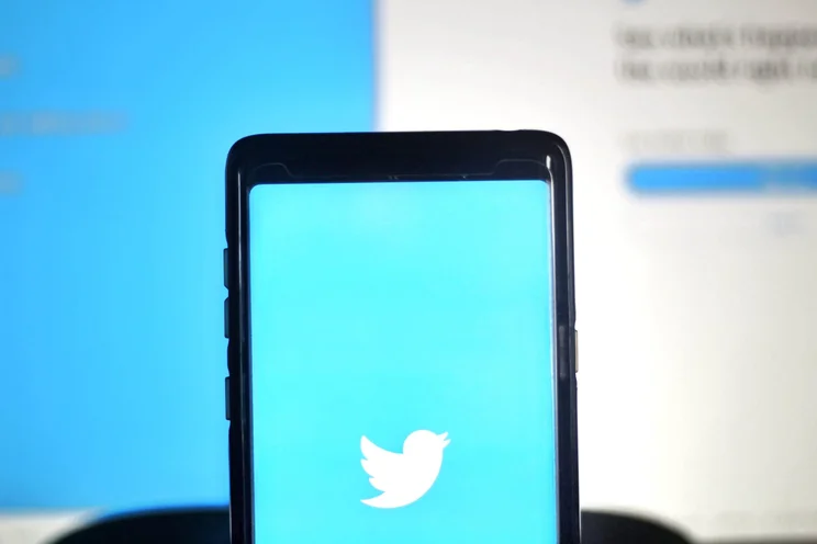 The Twitter logo on a smartphone, being held in front of a screen