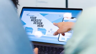 Two people gathered round a laptop with a website builder open on the screen. Source: Tech.co