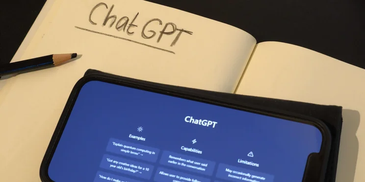 Smart phone with the online AI chat program ChatGPT. Notebook and pencil, ready to take notes for schoolwor