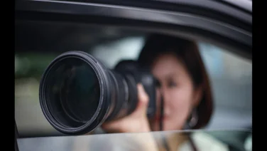A woman uses a large zoom camera out of a car window