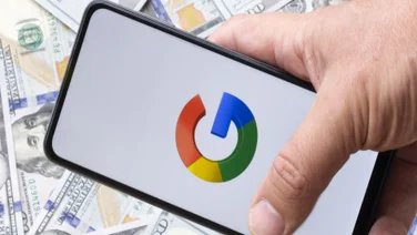 Google logo on a smartphone silhouette hold in hand. One hundreds dollar bills on the blurred background