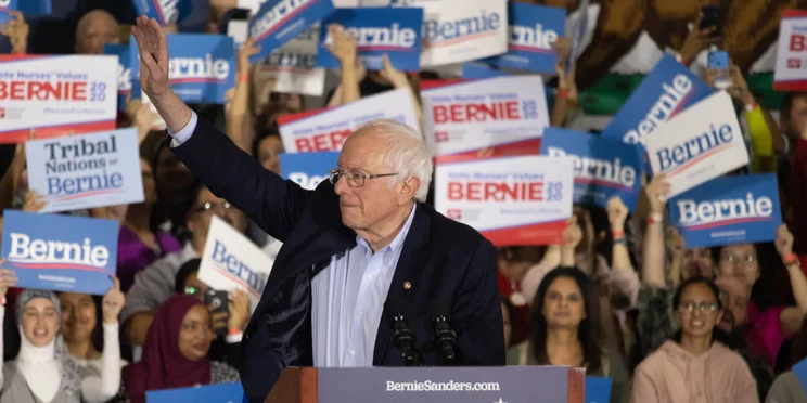 Bernie Sanders waving at a rally with supporters