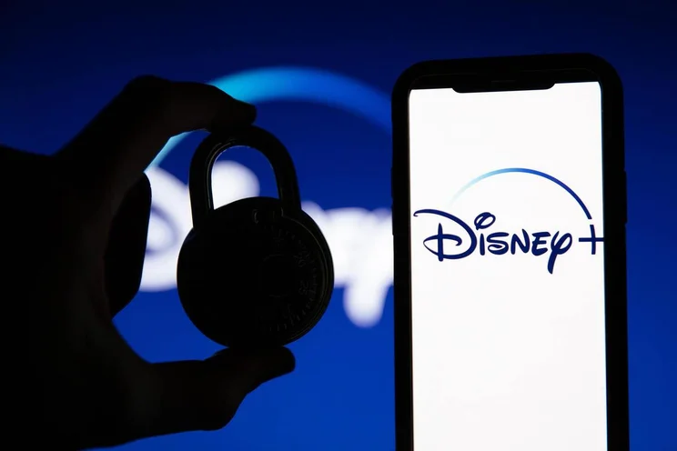 Disney + logo on a screen next to a hand holding a padlock