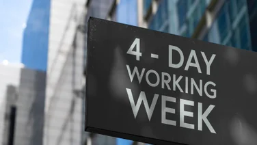 Sign displaying the words 4-day working week against a backdrop of downtown city buildings.