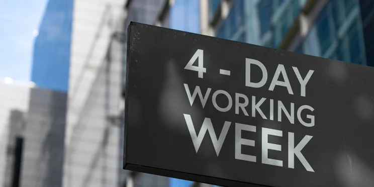 Sign displaying the words 4-day working week against a backdrop of downtown city buildings.