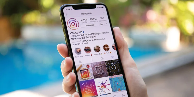 Woman holding an iPhone showing the Instagram app account