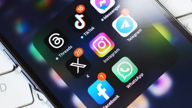 X app logo on a smartphone screen surrounded by other social media apps.