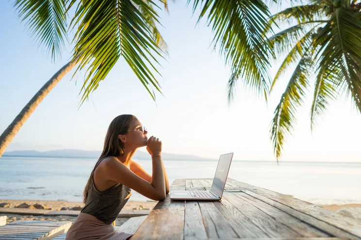 Female digital nomad working remotely from beach