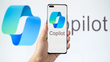 Hand holding smartphone featuring Microsoft Copilot logo against Copilot AI background