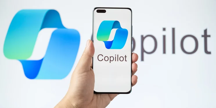 Hand holding smartphone featuring Microsoft Copilot logo against Copilot AI background