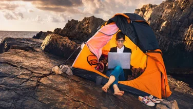 Woman sitting working remotely on laptop in tent on mountain
