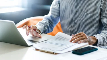 Man working at laptop with paperwork nearby illustrating how to create an asset tracking system