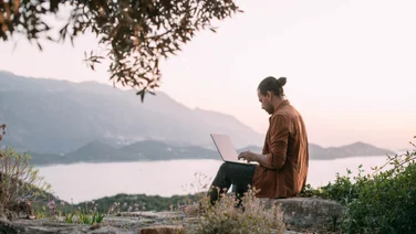 Man working remotely on laptop overlooking mountains and sea