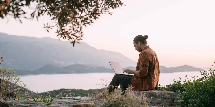 Man working remotely on laptop overlooking mountains and sea