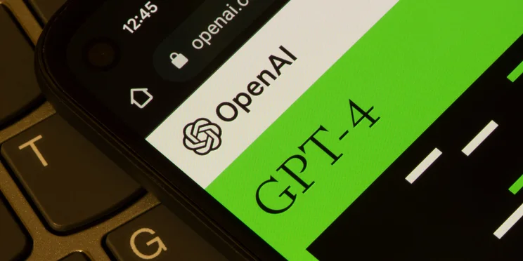 OpenAI and GPT-4 logos open on mobile screen on top of laptop keyboard