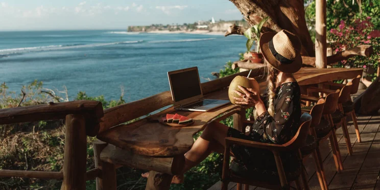 Woman in hat works from anywhere while drinking from coconut