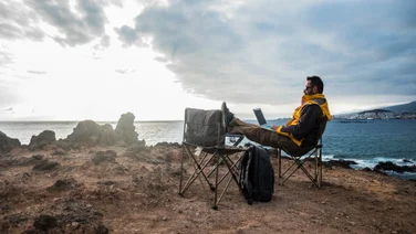 Man in rugged jacket works remotely on laptop sitting on cliff