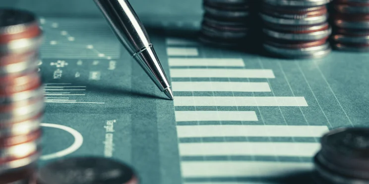 Pen on graph surrounding by coins suggesting tracking asset ROI