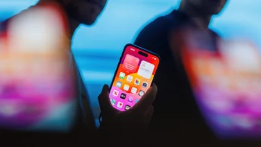Man holding iPhone 15 Pro against shadowy background illustrating iPhone spyware threat