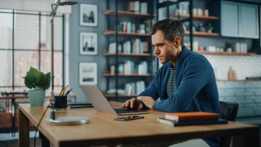 A man sitting at a desk looking at a laptop screen