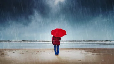 Person standing with an umbrella in the rain on a beach.