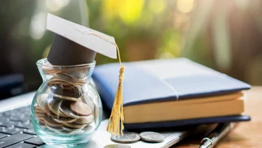 College student graduation gap on top of saving pot on laptop illustrating saving to pay student loan debt