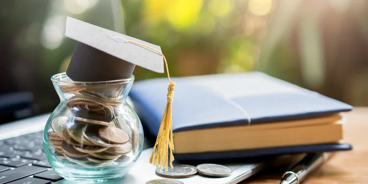 College student graduation gap on top of saving pot on laptop illustrating saving to pay student loan debt