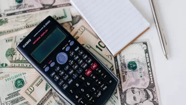 Dollar bills and calculator on a table.