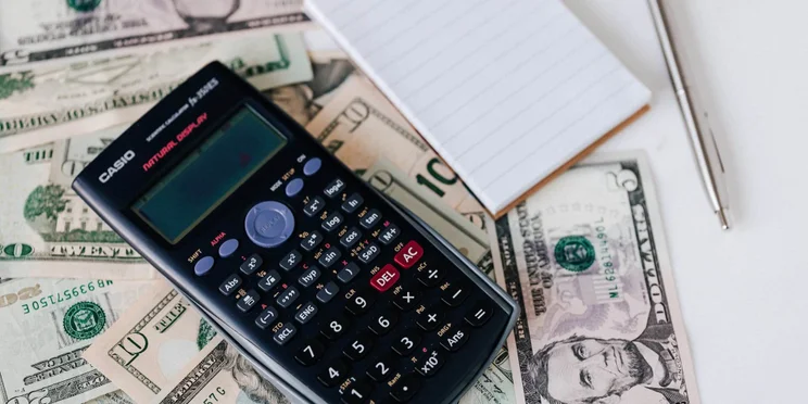 Dollar bills and calculator on a table.