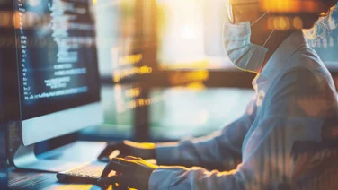 A woman wearing a COVID mask at the computer.