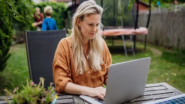 Woman remote working in her backyard with her two kids playing in the background.