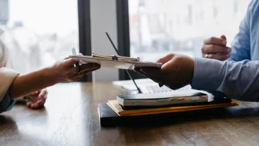 A recruiter hands a clipboard to a worker