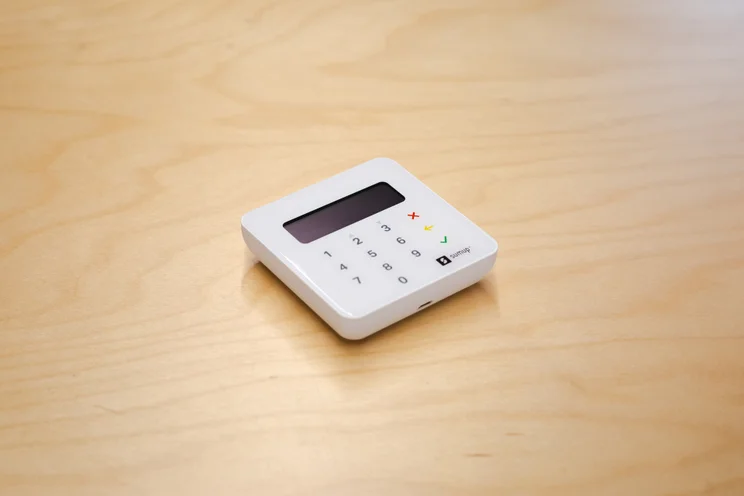 White SumUp card reader with display screen on wooden surface.