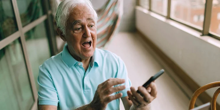 Older man looks at phone in shock