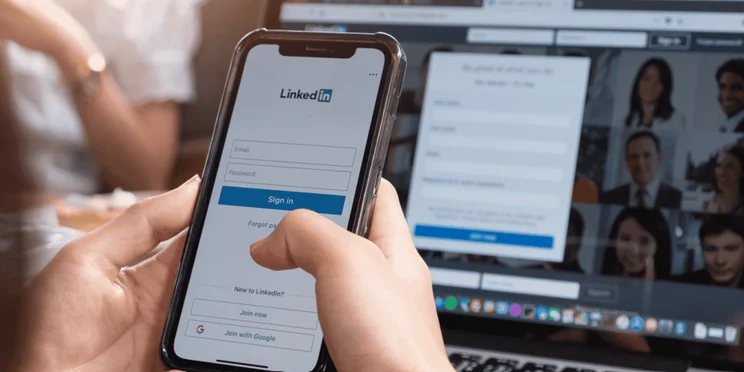 Linkedin app on a phone in front of a computer screen.