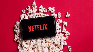 The Netflix logo, on a phone screen laid across popcorn.