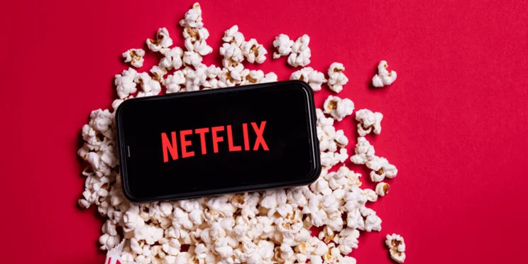 The Netflix logo, on a phone screen laid across popcorn.