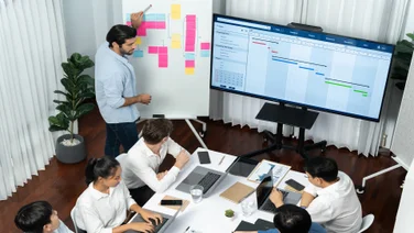 People working in a meeting room with person pointing at post-it notes