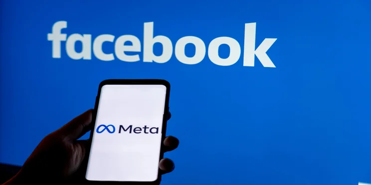 Person holding phone with Meta on screen in front of Facebook background