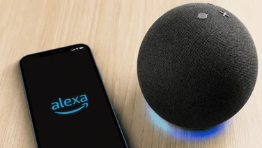 Alexa device next to phone with the Alexa app showing on the screen.