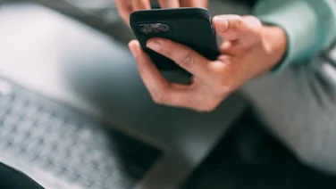 Someone holds a phone while on their laptop.