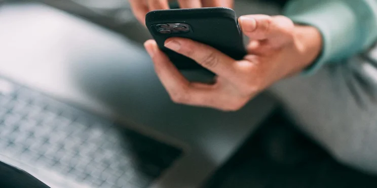 Someone holds a phone while on their laptop.